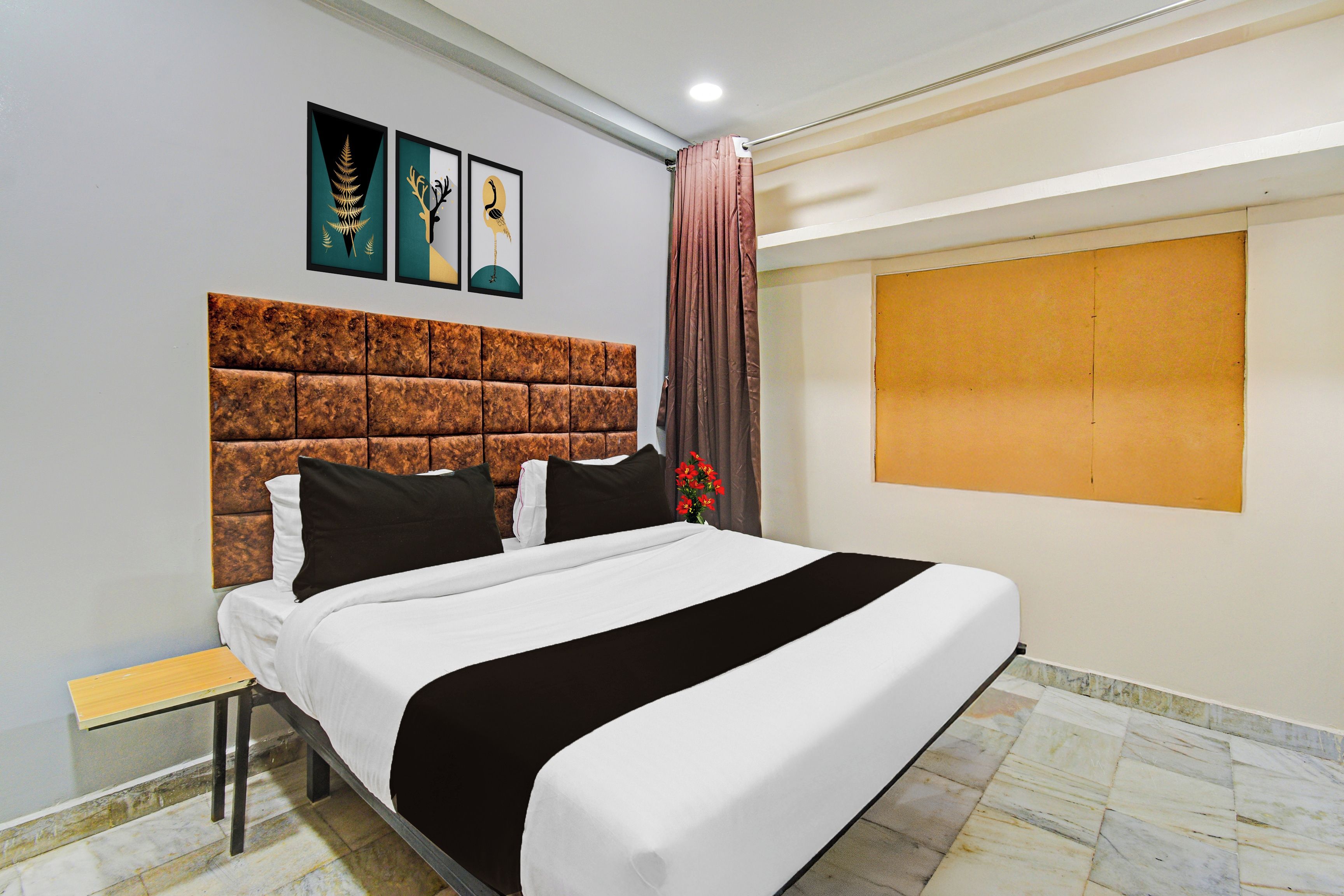 A hotel room with a large bed, a headboard, a nightstand, a wall-mounted TV, and artwork above the bed.