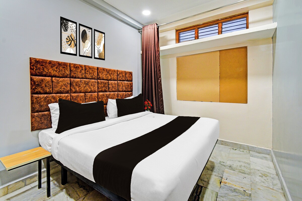 Habitación de hotel con una cama grande, cabecero, una mesita y un ventanal con cortinas.