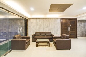 Un vestíbulo con pared de vidrio, un conjunto de sofá de cuero marrón, una mesa de centro de madera y una puerta de madera.