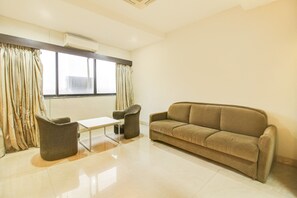 Una habitación con un sofá, dos sillones, una mesita y una ventana con cortinas.