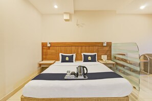 Habitación de hotel con cama, mesita de noche con teléfono, mampara de vidrio y bandeja con tetera y tazas.