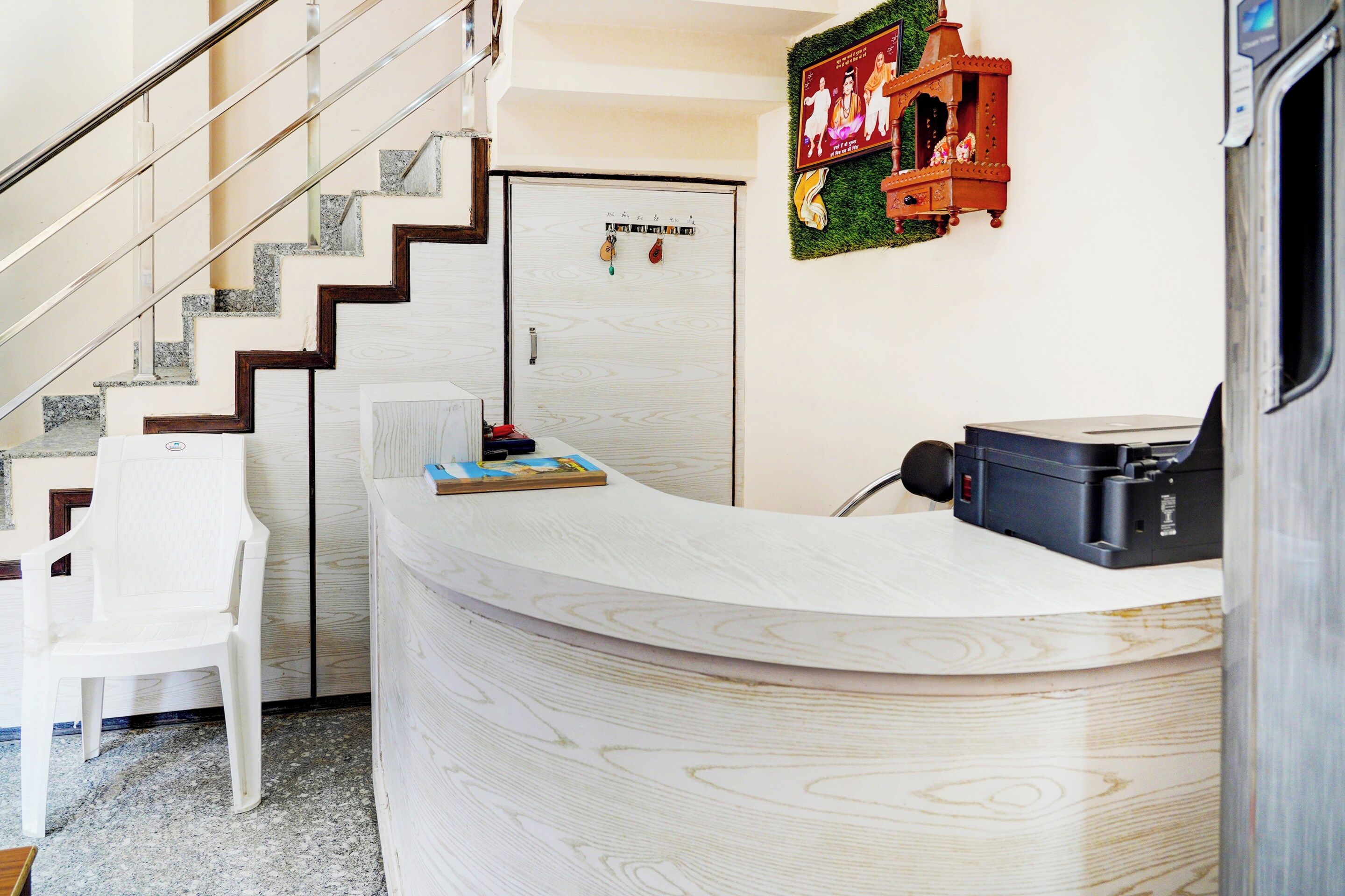 A reception desk with a curved design, a white chair, a staircase with a metal railing, and a door with a poster.