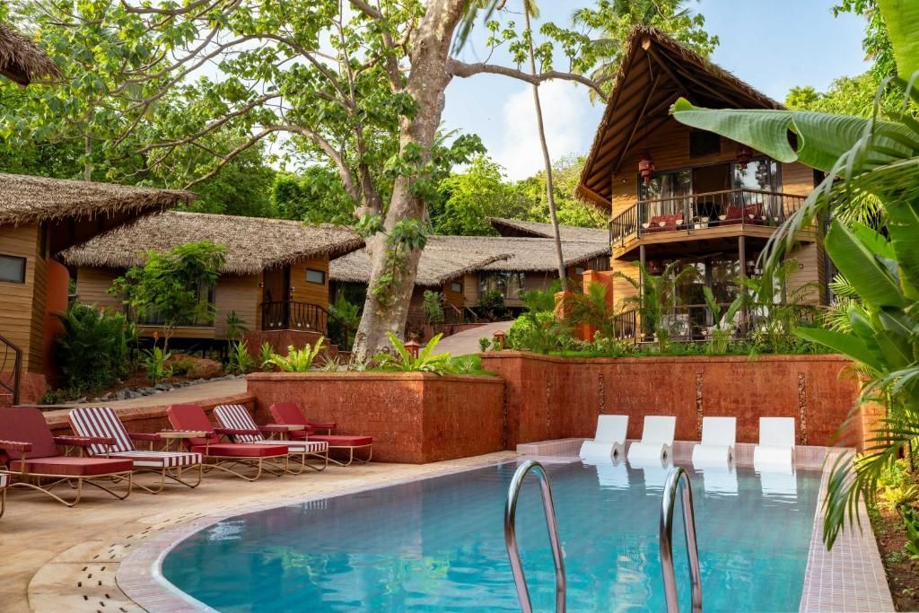 Un área de piscina con sillones de descanso, un edificio de madera con balcón y abundante vegetación.
