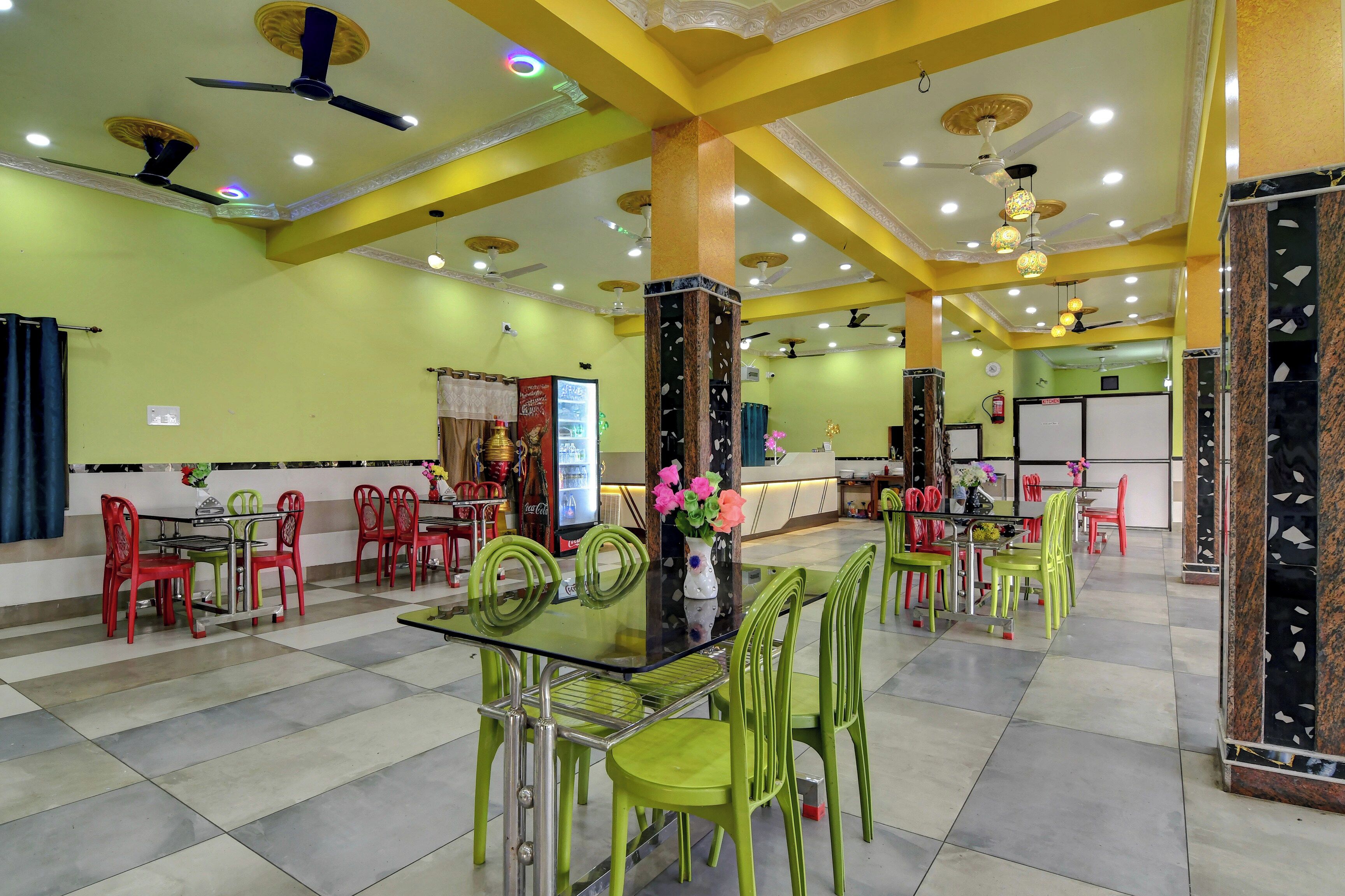 A restaurant with green and red chairs, a glass table, and ceiling fans.