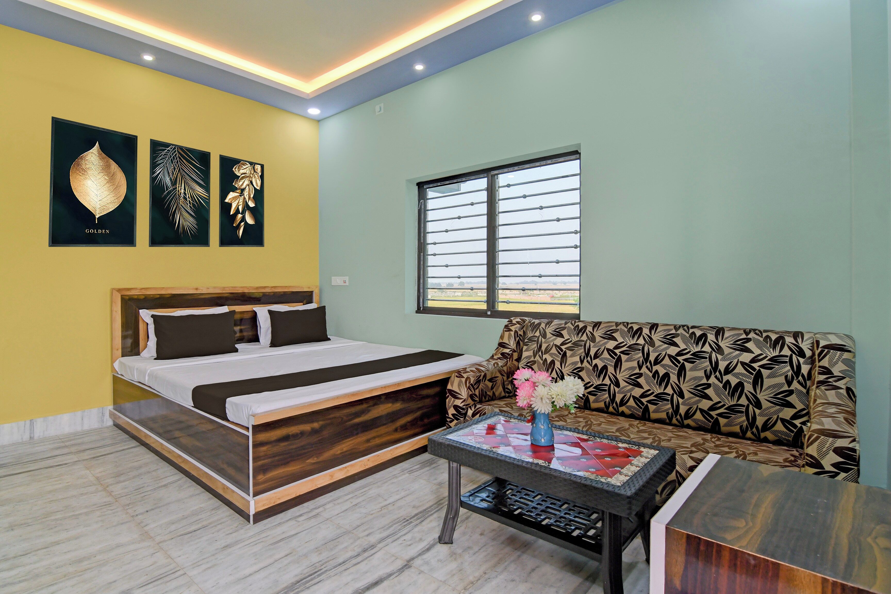 A hotel room with a bed, a sofa, a window, and artwork on the wall.