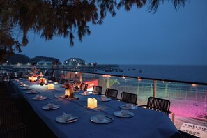 An outdoor dining area with tables set for a meal, overlooking a body of water and a distant building. - Meizhou Island Meiyu Xi'an Homestay (Putian)