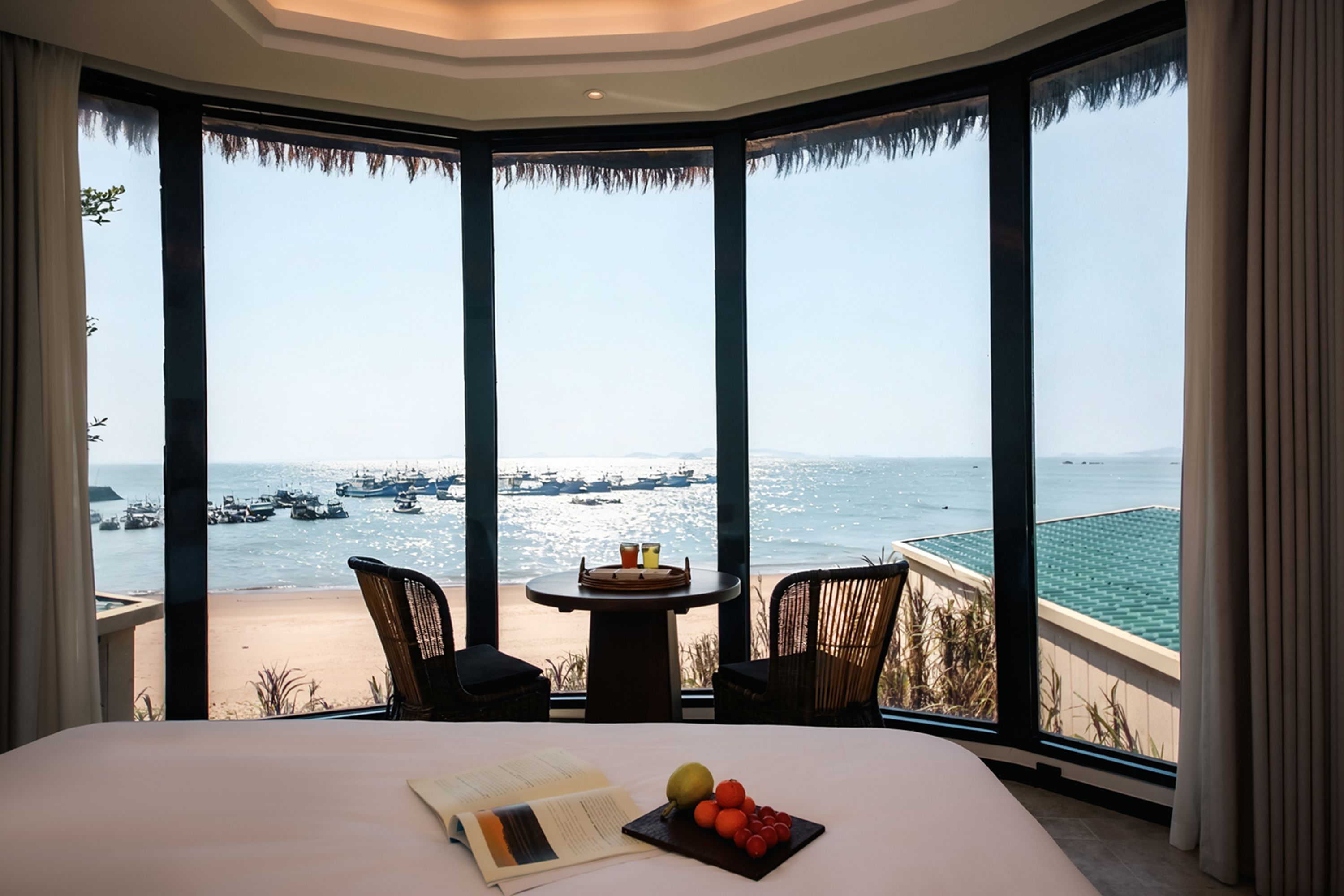 Habitación de hotel con una cama grande, una mesita con bebidas y vistas al mar con barcos.