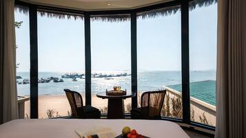 Habitación de hotel con una cama grande, una mesita con bebidas y vistas al mar con barcos.