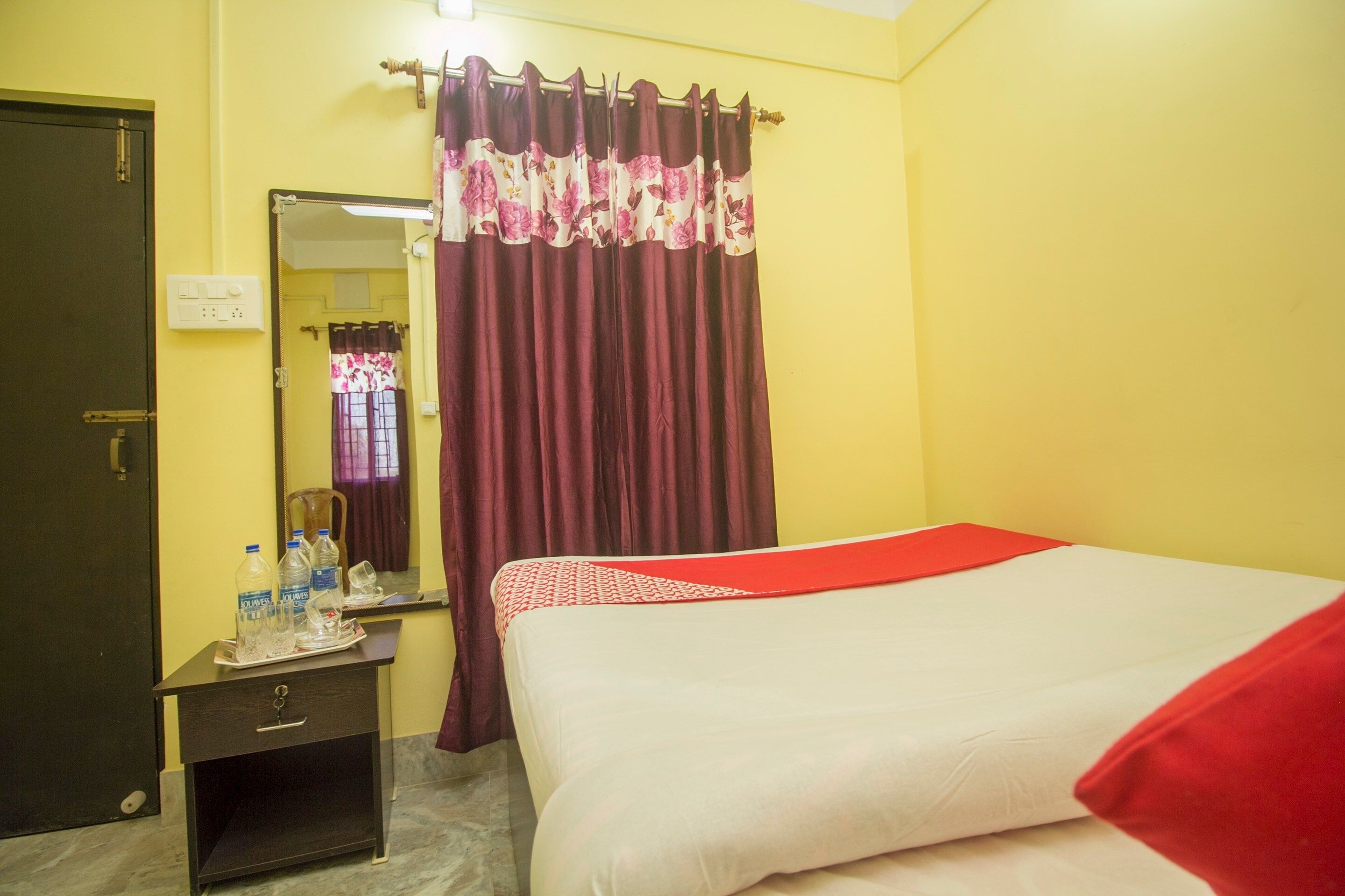 A hotel room with a bed, a bedside table, a mirror, a wardrobe, and a curtain.