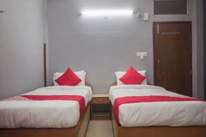 A hotel room with two single beds, each with white bedding and red pillows, a small bedside table, a wooden wardrobe, and a light fixture on the ceiling. - Hotel O Golden Moments (Siliguri)
