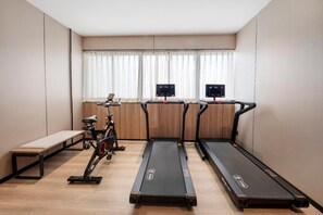 Une salle équipée de trois tapis de course, d’un vélo d’appartement et d’un banc de musculation.