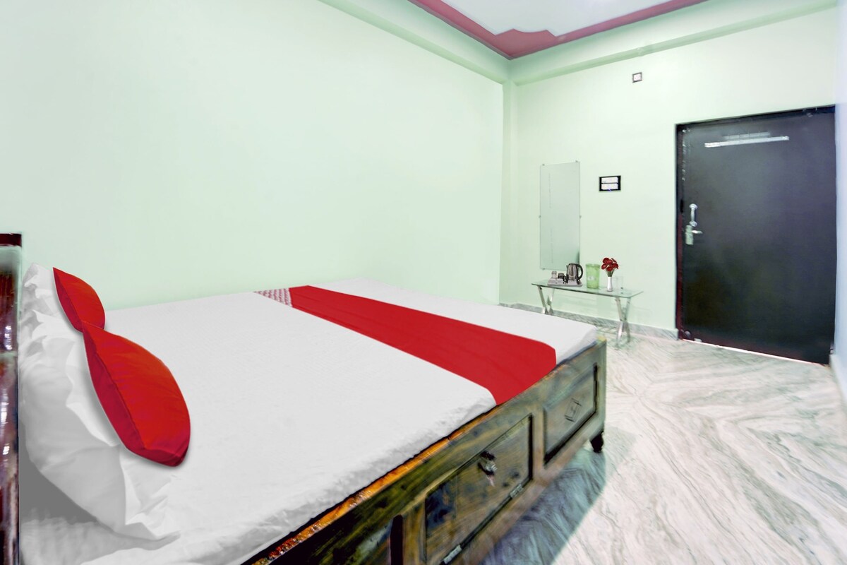 A room with a bed, a dresser, a mirror, a door, and a small table with a vase of flowers.