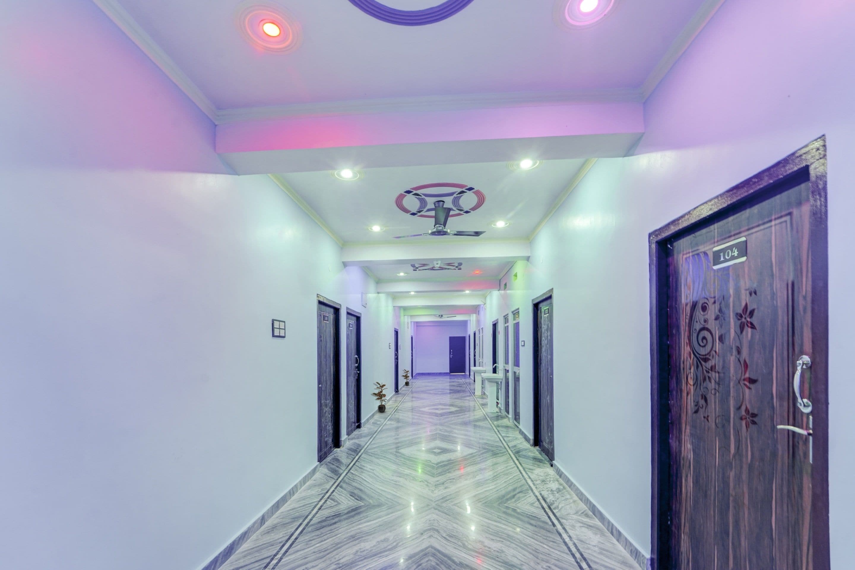 Un pasillo de hotel con piso de mármol, luces de techo y un ventilador de techo.
