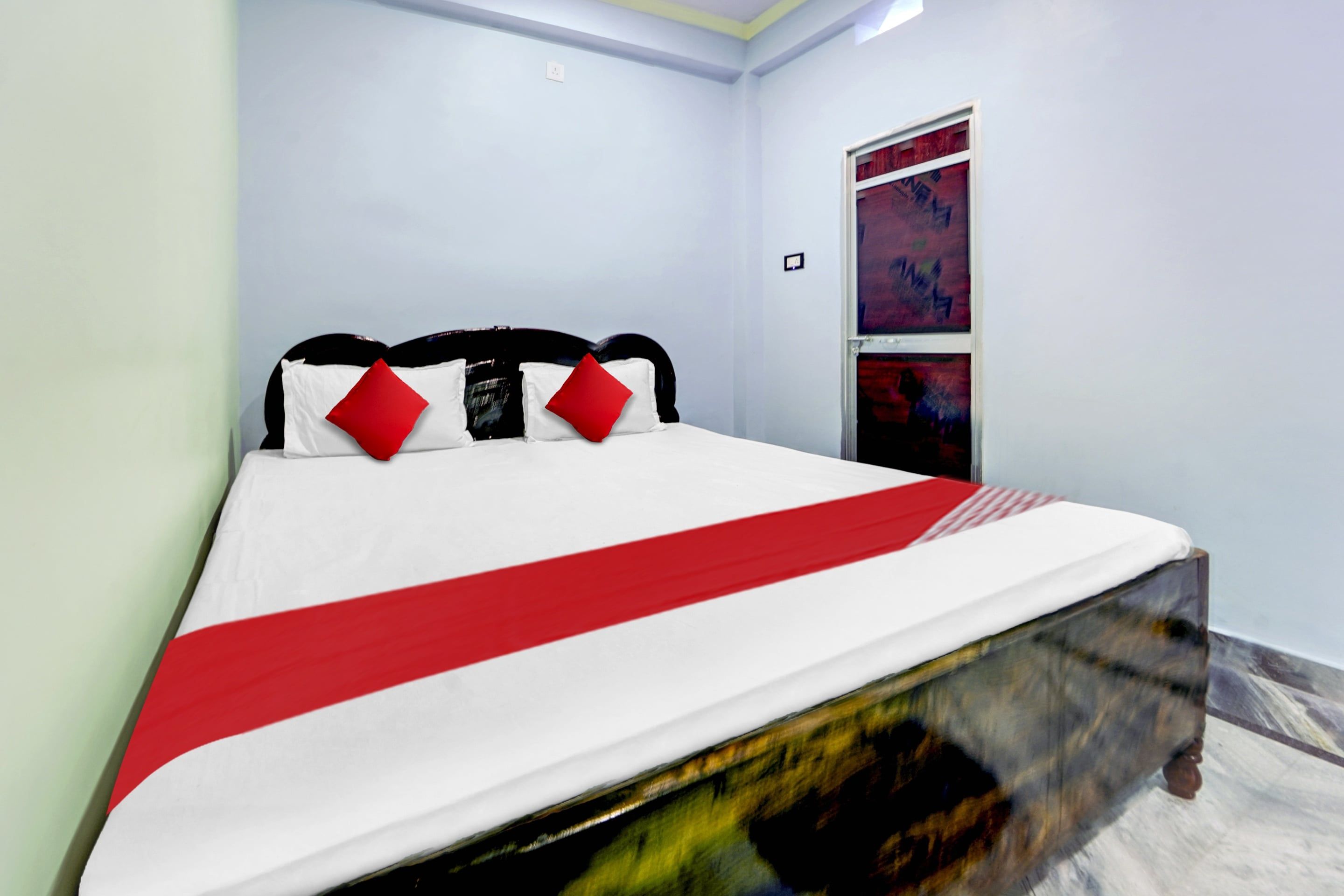 Un lit avec une couvre-lit blanche et rouge, une tête de lit noire et des oreillers rouges.