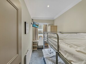 Habitació d'hotel estreta amb un llit superposat, televisió penjada a la paret, radiador i finestra amb cortines.