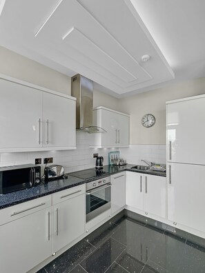 A modern kitchen with white cabinets, a stainless steel range hood, a microwave, a toaster, and a clock on the wall. - Granada Apartments Burbage flat 4 1st floor sea view (Blackpool FY2 9JS)