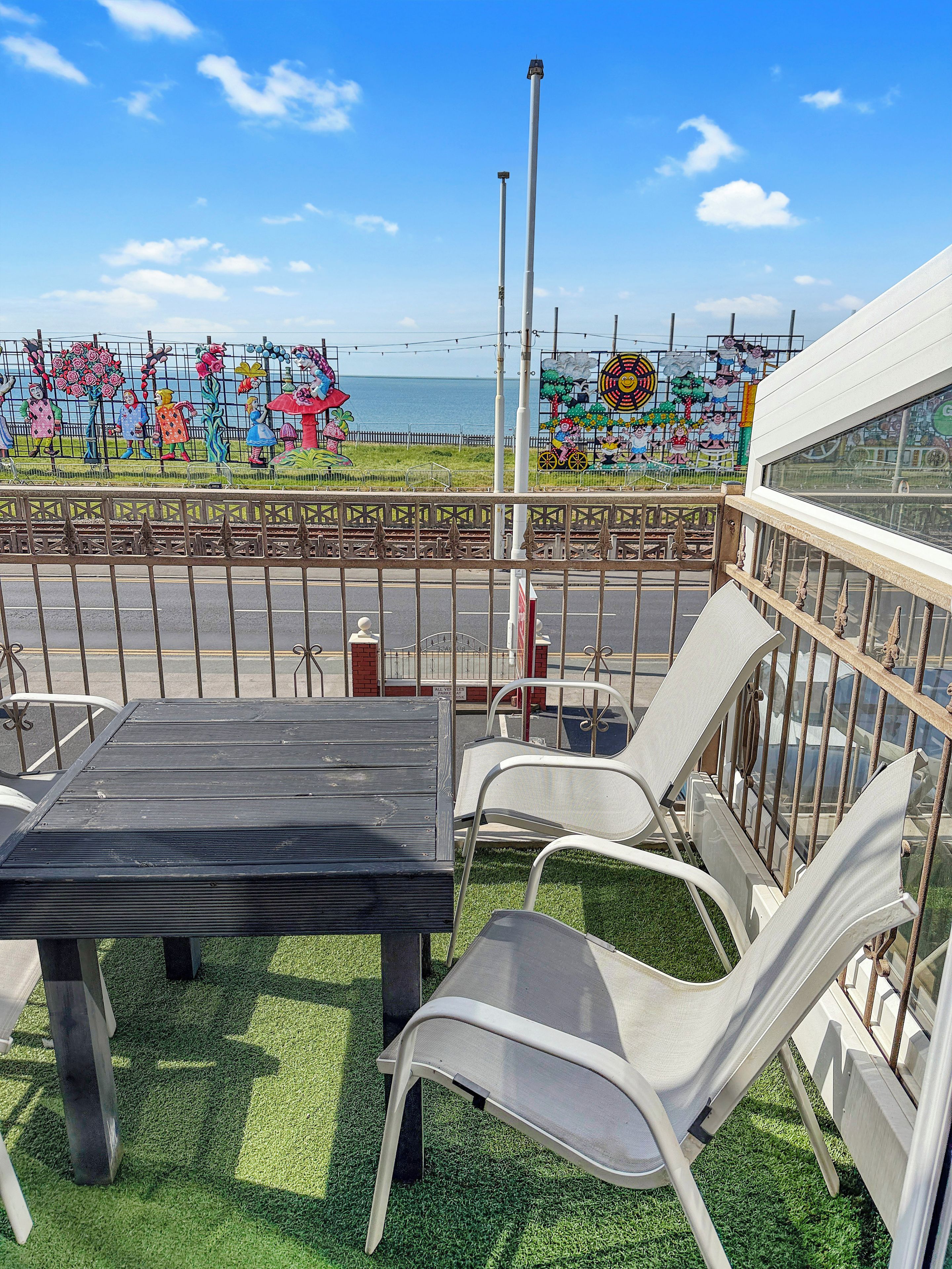 A balcony with a table and chairs, a view of the sea, and a colorful mural in the background.