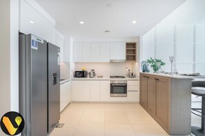 A modern kitchen with white cabinets, a stainless steel refrigerator, a built-in oven, and a microwave. - Vogue | Downtown with Easy Access to Dubai Mall (Dubai)
