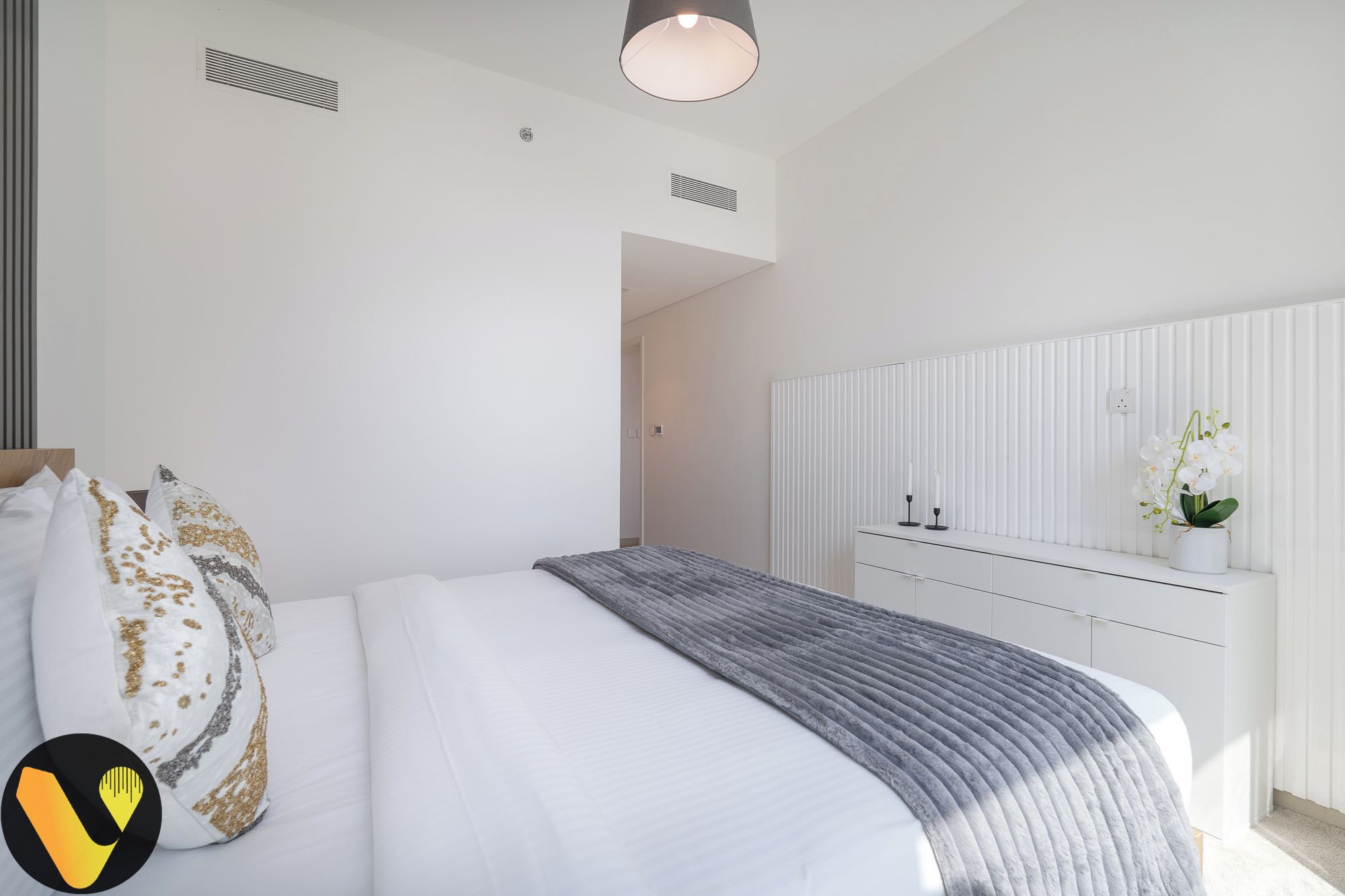 A modern bedroom with a bed, white walls, a white wardrobe, and a bedside table with a vase of flowers.