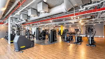 Un gimnasio con diverso equipo de ejercicio, incluyendo cintas de correr y máquinas de pesas, y un suelo de madera pulida.