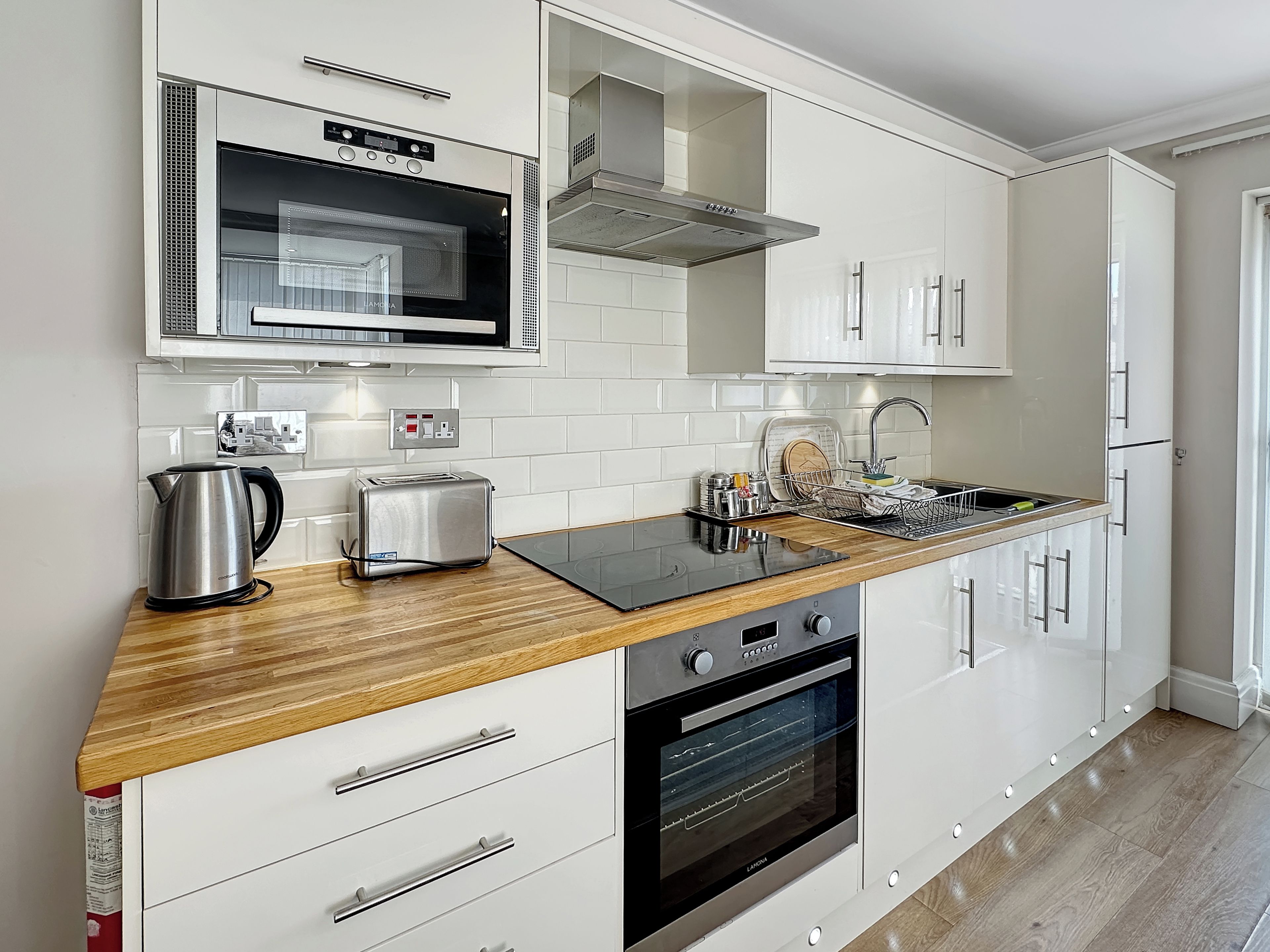 A modern kitchen with white cabinetry, a stainless steel toaster, a kettle, and a built-in oven.