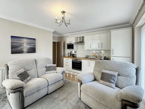Een moderne woonkamer met twee grijze banken, een grijs vloerkleed en een keuken op de achtergrond.