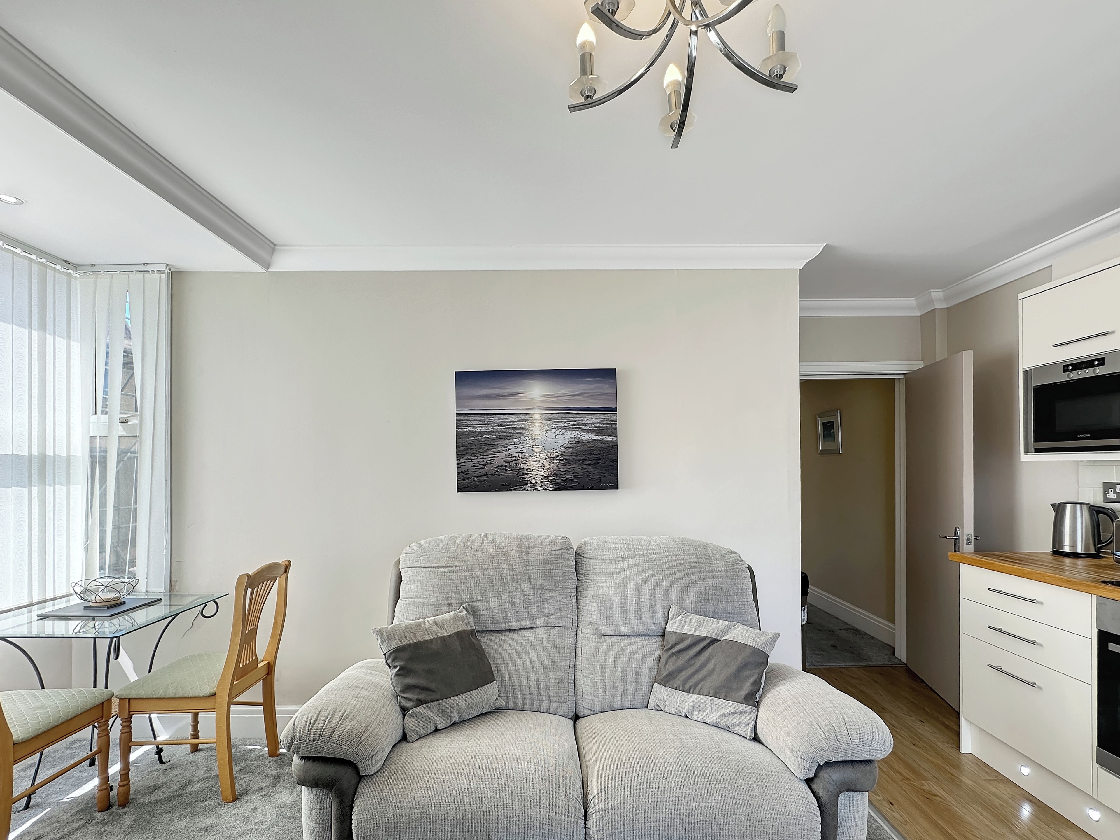 A modern living room with a grey sofa, a dining table, and a kitchen area.
