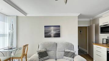 A modern living room with a grey sofa, a dining table, and a kitchen area.