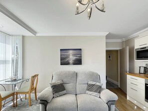 A modern living room with a grey sofa, a dining table, and a kitchen area. - Granada Apartments Burbage flat 3 1st floor rear (Blackpool FY2 9JS)