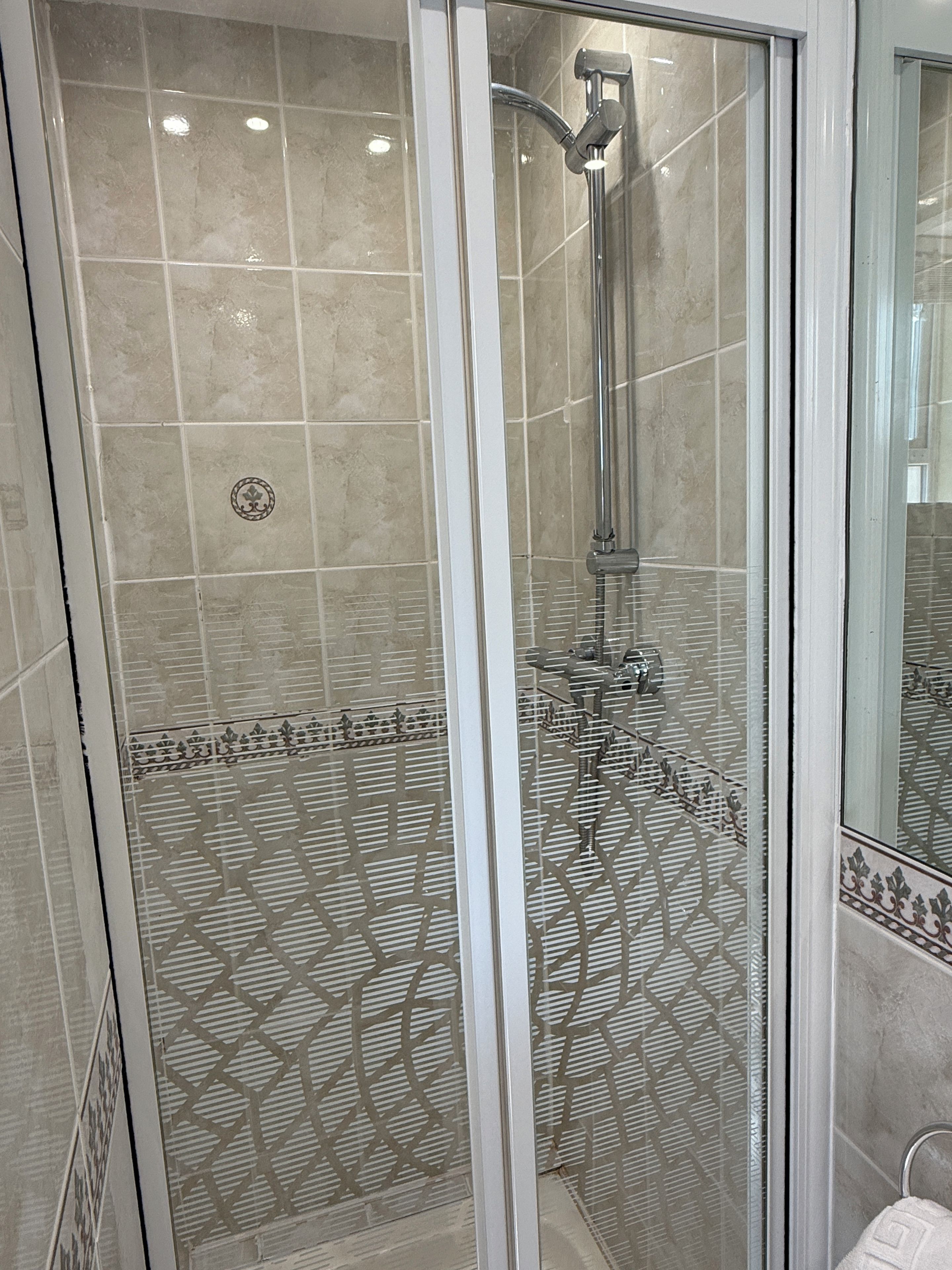 A glass-enclosed shower with a showerhead and control panel.