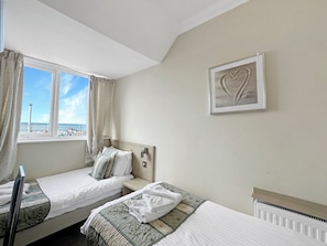 Une chambre d’hôtel avec deux lits, une fenêtre avec des rideaux, un radiateur et un tableau encadré au mur.