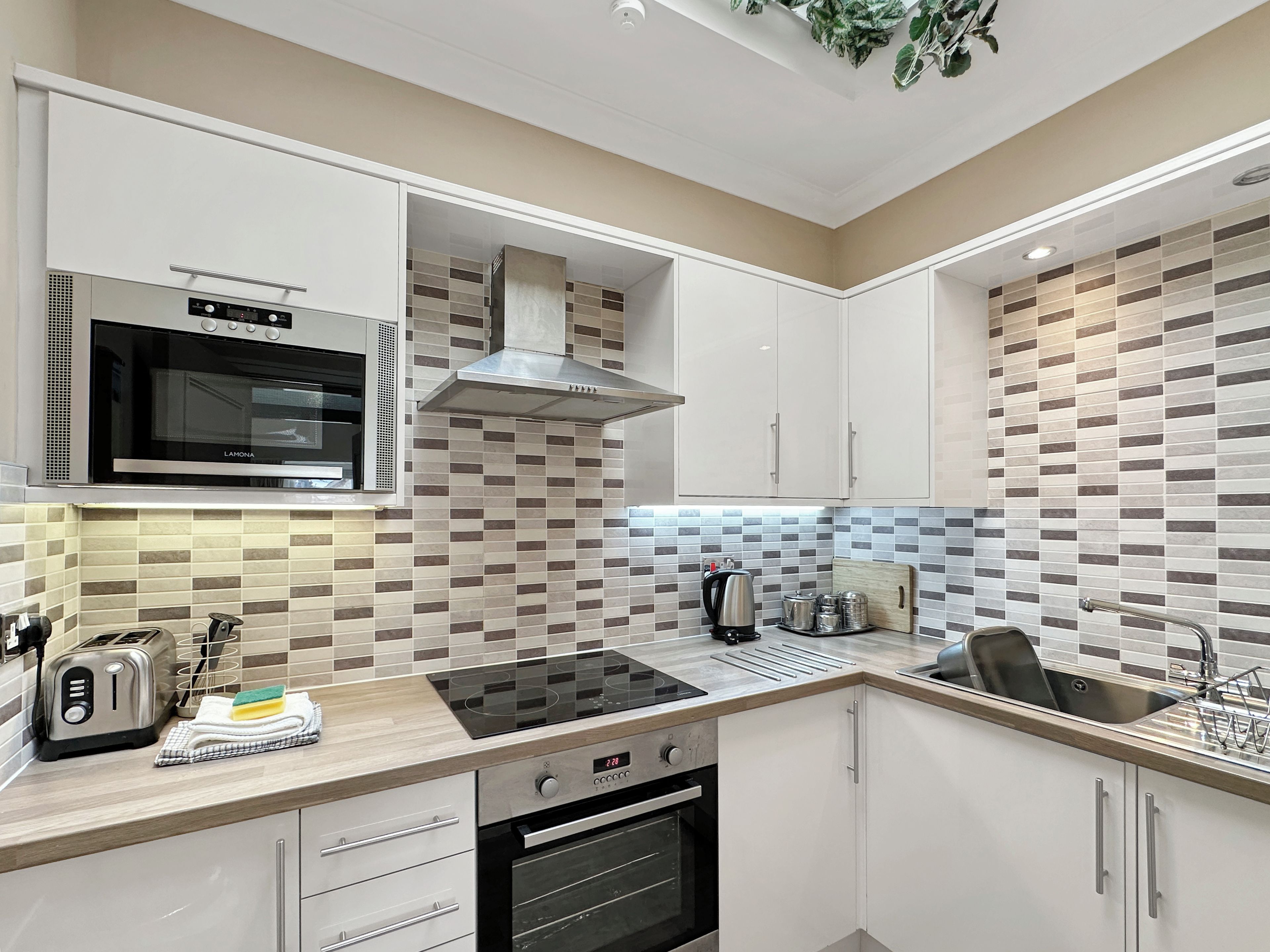 A modern kitchen with a built-in microwave, stove, oven, and a kettle on the countertop.