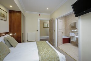 A hotel room with a bed, a television, a bathroom with a sink and mirror, and a door leading to another room. - Granada Apartments Burbage flat 2 ground floor sea view (Blackpool FY2 9JS)