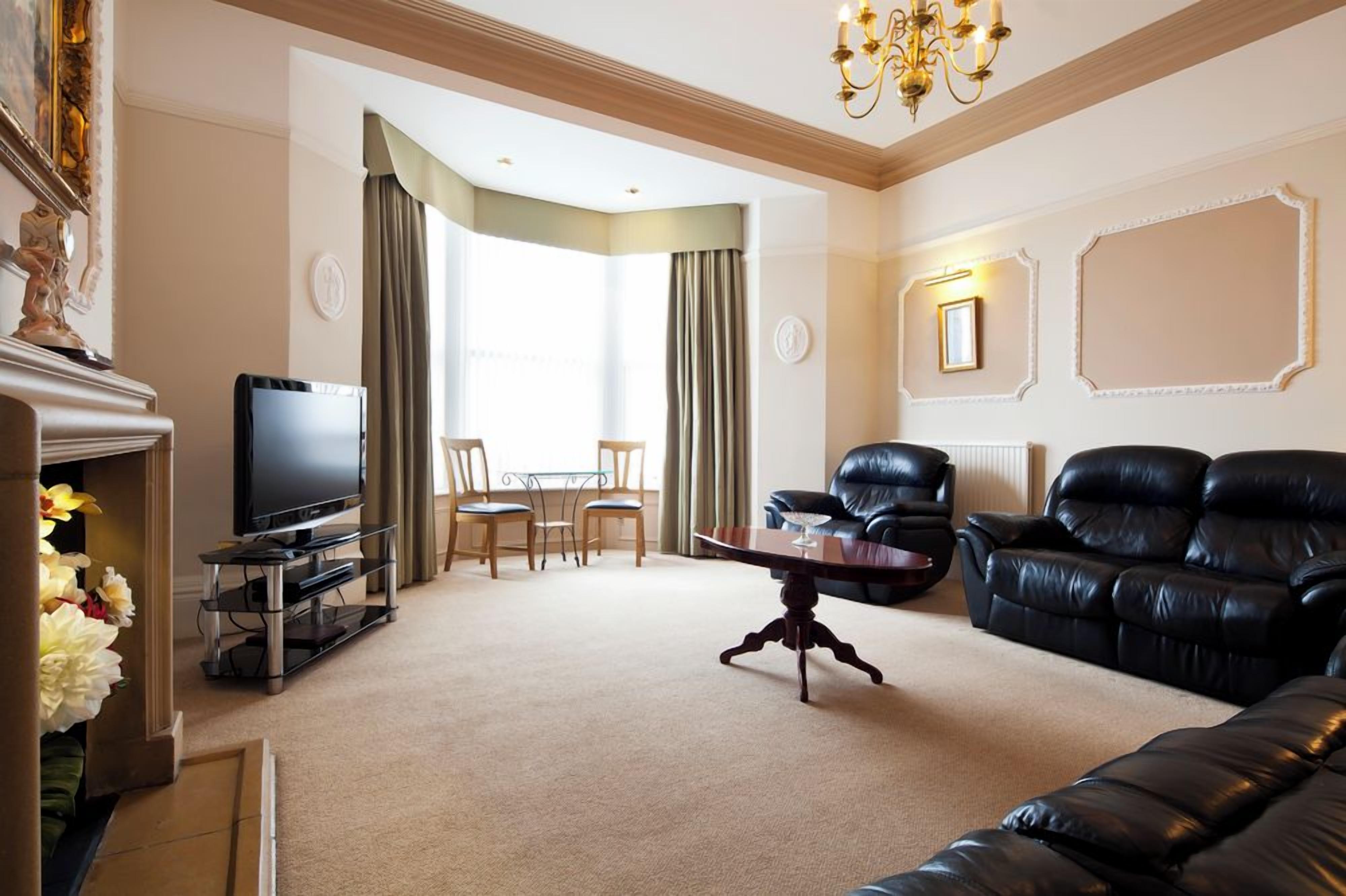 A living room with a television, leather sofa, dining table, and chairs.