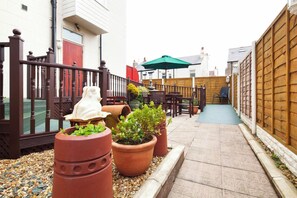 A narrow outdoor patio with a wooden fence, a red door, and a green umbrella. - Granada Apartments Burbage flat 2 ground floor sea view (Blackpool FY2 9JS)