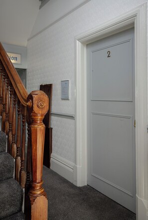A hallway with a wooden staircase, a white door with the number 2, and a wall-mounted sign. - Granada Apartments Burbage flat 2 ground floor sea view (Blackpool FY2 9JS)