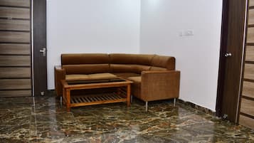 Een hoekappartement met een bruine bank, een houten salontafel en een betegelde vloer.