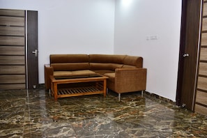 Una habitación de esquina con un sofá marrón, una mesa de centro de madera y suelo de baldosas.