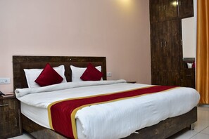 Una cama con cabecera de madera, ropa de cama blanca y detalles en rojo.