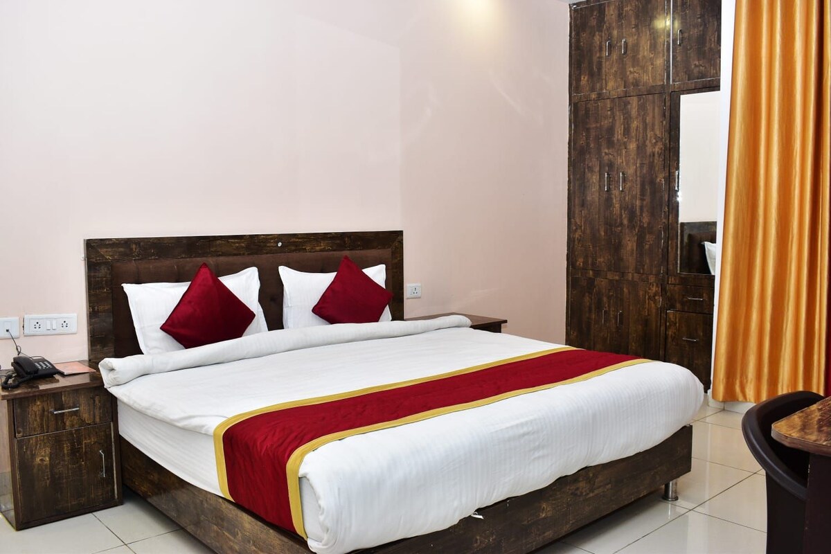 Una habitación de hotel con cama de madera, ropa de cama blanca, detalles en rojo y amarillo, una mesita de noche de madera y un espejo grande.