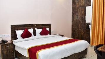 Une chambre d’hôtel avec un lit en bois, du linge de lit blanc, des touches de rouge et de jaune, une table de chevet en bois et un grand miroir.