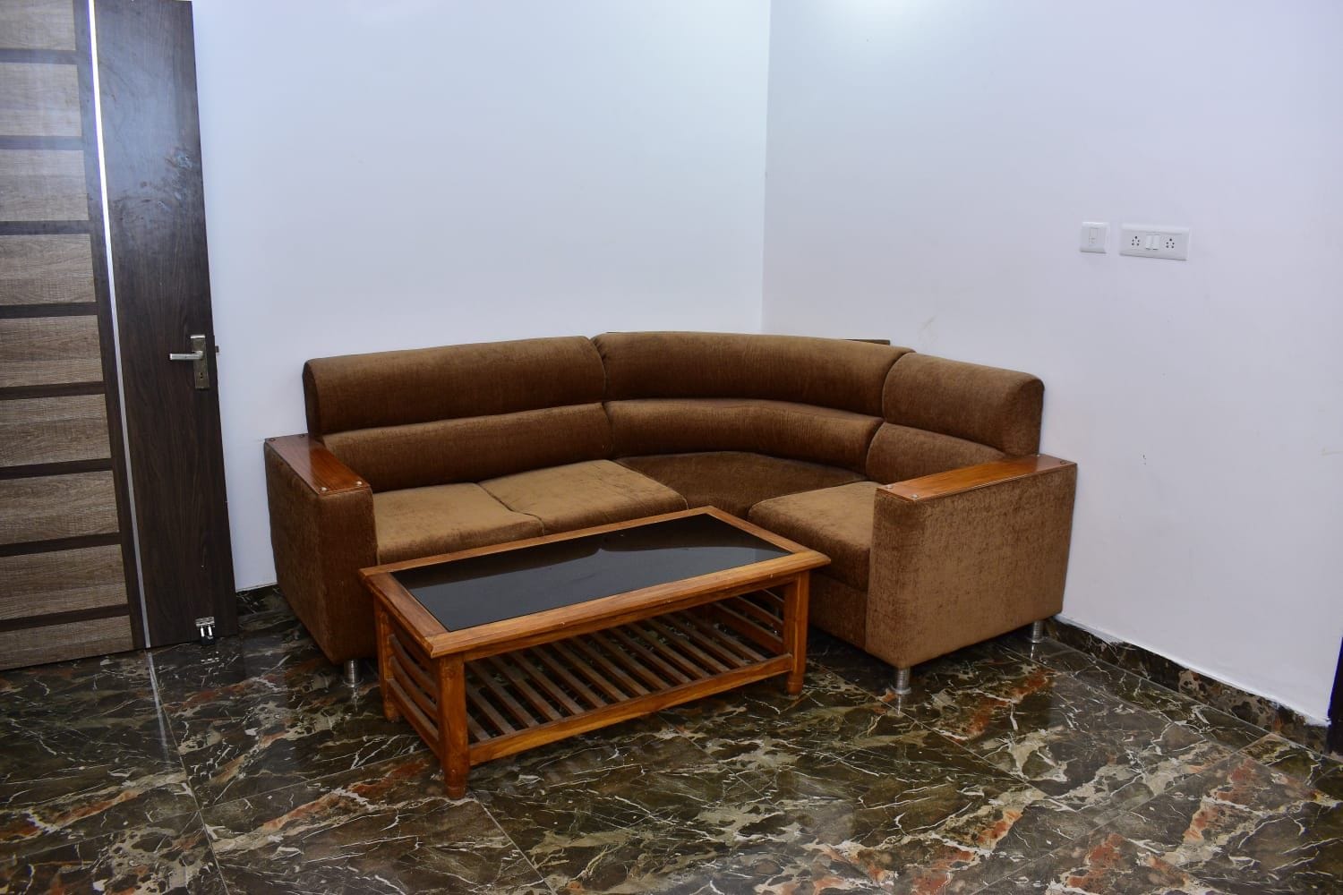 Une pièce d’angle avec un canapé d’angle marron, une petite table basse en bois et un sol en marbre.