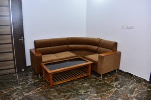 Una habitación de esquina con un sofá seccional marrón, una pequeña mesa de centro de madera y un piso de mármol.