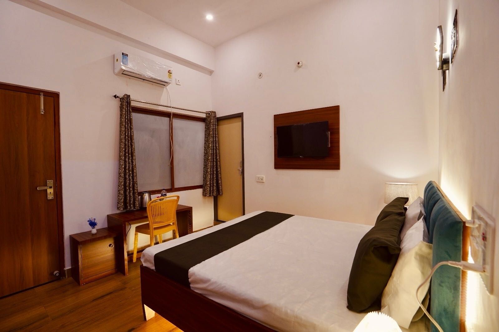 A hotel room with a bed, a desk, a chair, an air conditioning unit, a television, and a window with curtains.