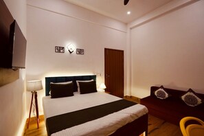 A hotel room with a bed, bedside lamp, wall art, a wooden door, and a red sofa with cushions. - Hotel O 7 Orchid (Sultanpur)