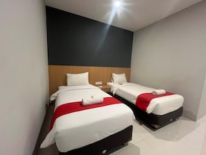 Habitación de hotel con dos camas, cada una con ropa de cama blanca y detalles rojos, cabeceros de madera y un diseño moderno.