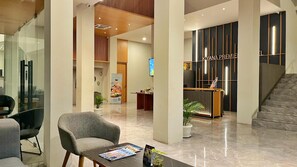 Un vestíbulo de hotel con mostrador de recepción, zona de estar y una escalera.