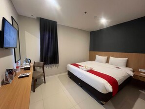Una habitación de hotel con cama, escritorio, silla, televisor y ventana con cortinas.