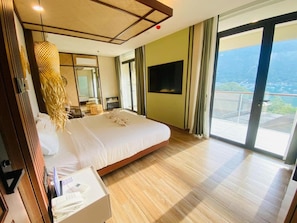 Quarto de hotel com uma cama grande, televisão de tela plana, varanda com vista e piso de madeira.