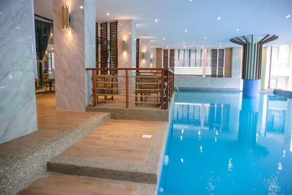 Piscina com degraus de acesso, emoldurada por um interior moderno com paredes de mármore e detalhes em madeira.